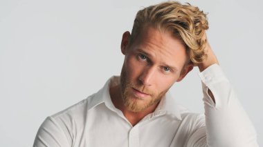 Yakışıklı, sarışın, sakallı adam beyaz arka planda izole edilmiş kameraya bakıyor. Gömlekli genç işadamı