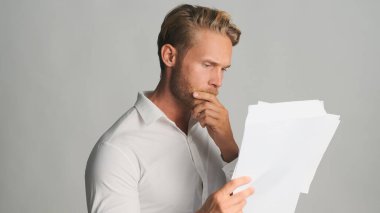 Gömlekli, sarışın ve sakallı genç bir işadamı beyaz arka planda izole edilmiş ciddi bir şekilde kitap okuyor. İş konsepti