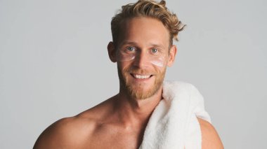 Göz bantları ve omuzlarında havluyla beyaz arka planda gülümseyen çekici sarışın sakallı adam.