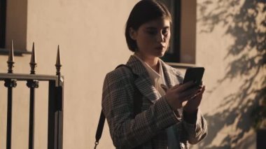 Şehir caddesinde taksi beklerken akıllı telefondan mesaj yazan modern iş kadını.