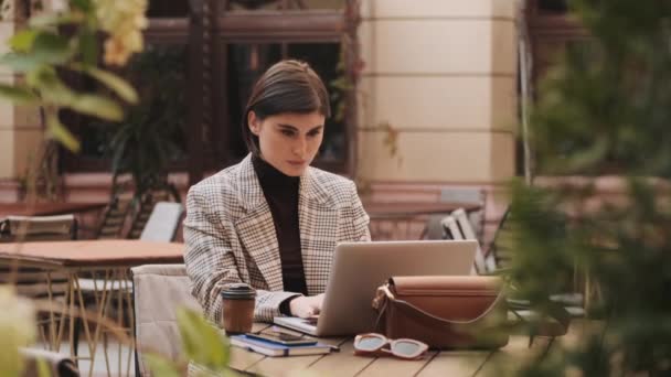 在笔记本电脑上工作的年轻而时尚的女商人坐在咖啡店的庭院里喝咖啡 — 图库视频影像