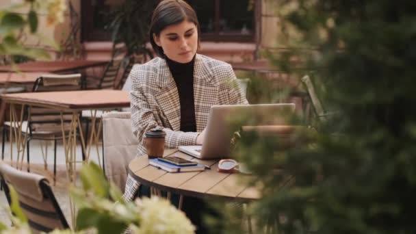 カフェの屋外でコーヒーブレイク中にラップトップで働く上での仕事の問題を解決する美しいスタイリッシュなビジネス女性 — ストック動画