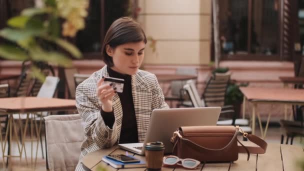 通过信用卡追踪一位漂亮女士在网上购物的照片 年轻的女商人在户外咖啡店用笔记本电脑上网付款 — 图库视频影像