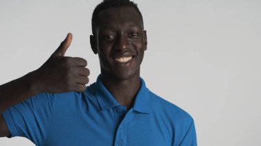 Genç, Afro-Amerikalı, beyaz arka planda baş parmağını gösterip gülümsüyor. İşaret gibi