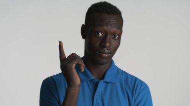 Sıradan giyinmiş Afro-Amerikalı adam işaret parmağını kaldırıyor ve beyaz arka planda kamerada yeni bir fikir gösteriyor. Düşünme ifadesi
