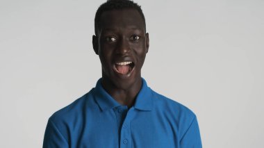 Sıradan giyinmiş heyecanlı bir Afro-Amerikalı beyaz arka planda izole edilmiş kameraya hayret ediyor. Vay canına. 