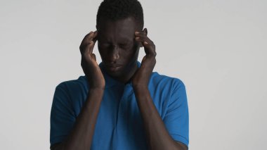 Beyaz arka planda, baş ağrısından parmaklarını şakaklara bastıran yorgun, Afrikalı Amerikalı genç bir adam.