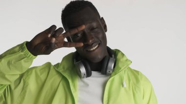 Beyaz arka planda, parlak ceketli, kulaklıklı, yakışıklı, Afro-Amerikan bir adam. Arkadaş canlısı adam.
