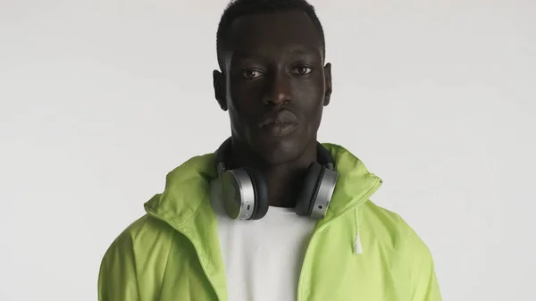 Stylowy Afroamerykanin Jasnej Kurtce Słuchawkami Wyglądającymi Poważnie Aparacie Odizolowanym Białym — Zdjęcie stockowe
