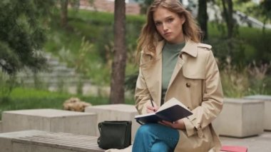 Güzel bir öğrencinin kameraya gülümseyen fotoğrafını çekerken günlüğe notlar yazıp üniversitede ödev yaparken parkta bir bankta.