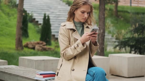 Schöne Studentin Trenchcoat Die Ernst Liest Vorlesung Auf Dem Smartphone — Stockvideo