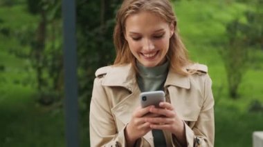 Güzel bir kız öğrencinin mutlu bir şekilde erkek arkadaşıyla akıllı telefondan sohbet ederken ve parkta sırıtırken görüntülerini izliyordum.