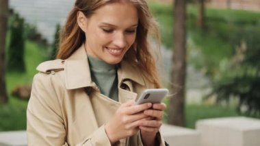 Sınav notlarını akıllı telefondan alan güzel sarışın kız öğrenciyi kapat ve mutlu bir şekilde dışarıda gülümse.