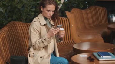 İyi görünümlü bir kızın sokak kafesinde oturup sosyal paylaşım ağı izlerken ve ders arası sırasında kahve içerken görüntüsünü kaydetmek.
