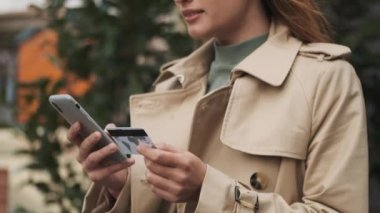 Çevrimiçi alışverişleri ödeyen şık bir kadın kredi kartıyla dışarıda akıllı telefon kullanıyor.