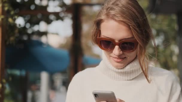 Güneş Gözlüklü Beyaz Kazaklı Güzel Bir Kız Sokakta Akıllı Telefondan — Stok video