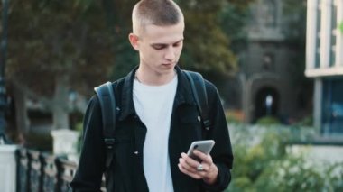 Şehir caddesi boyunca üniversiteye gitmek için akıllı telefon kullanan çekici modern öğrenci. İnternet iletişim kavramı