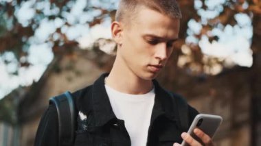 Üniversiteye giderken akıllı telefondan ders programına bakan yakışıklı bir öğrencinin portresi.