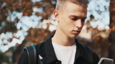 Üniversiteye giderken akıllı telefon kullanan yakışıklı öğrencinin portresi. Dışarıdaki genç öğrenci.