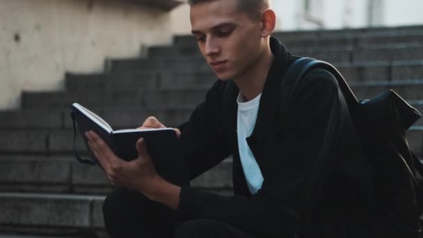 Portret Atrakcyjnego Studenta Wyglądającego Pewnie Piszącego Notatniku Podczas Nauki Schodach — Wideo stockowe