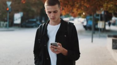 Yakışıklı öğrenci, üniversiteye giderken akıllı telefon kullanarak sosyal ağlara kayıyor. Dışarıdaki genç öğrenci.