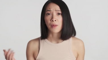 Genç Asyalı kadın üzgün görünüyor, kendini işaret ediyor ve beyaz arka planda izole edilmiş kamerada hiçbir hareket göstermiyor.