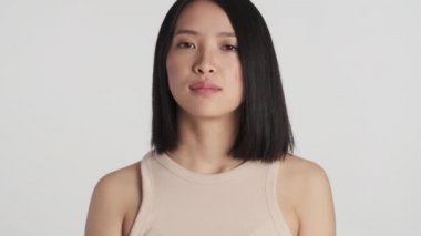 Genç ve güzel Asyalı kadının portresi kameraya dikkatlice bakıyor beyaz arka planda kendini güvende hissediyor. Yüz ifadesi