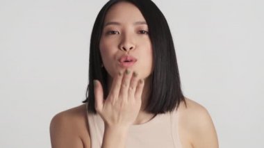Güzel Asyalı kız beyaz arka planda izole bir şekilde kameraya hava öpücüğü gönderiyor. Çekici bir kadın stüdyoda poz veriyor.