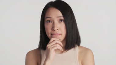 Düşünceli Asyalı kız elini çenesine koyuyor ve beyaz arka planda izole edilmiş kameraya hayır diyor. Yüz ifadesi