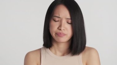 Üzgün Asyalı kız arkadaşına saldırmış. Üzücü bir şekilde beyaz arka planda yalnız poz vermiş.