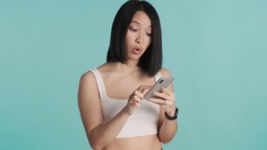 Akıllı telefonlara odaklanmış güzel Asyalı kız mavi arka planda izole edilmiş malları internetten seçiyor. Modern teknoloji kavramı
