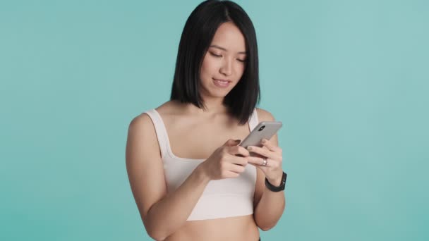 魅力的なアジアの女の子とともにボブの髪は青の背景にスマートフォンを使用してソーシャルネットワークを閲覧 — ストック動画