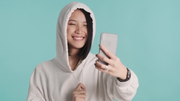 후드를 배경으로 스마트폰으로 귀여운 셀카를 아시아 — 비디오