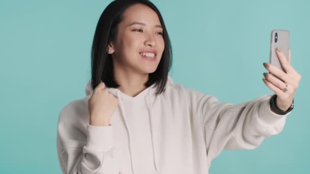 Kapüşonlu Giyinmiş Çekici Asyalı Kız Mavi Arka Planda Akıllı Telefon — Stok video