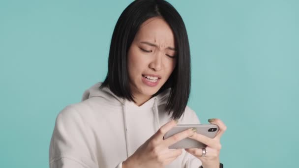 매력적 신경이 아시아 소녀는 배경을 온라인 경쟁에 참여하는 스마트폰상에서 감정적으로 — 비디오