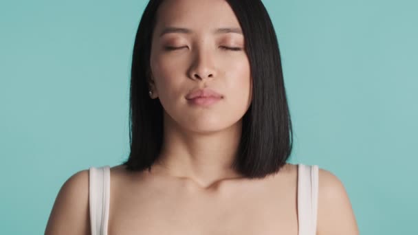 紧闭美丽沉稳的亚洲女孩深深地吸了一口气 闭着眼睛 与蓝色背景隔离 冥想的概念 — 图库视频影像