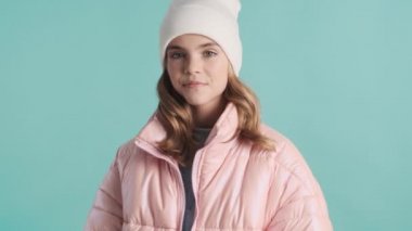 Pembe ceketli ve şapkalı güzel bir genç kız mavi arka planda gülümsüyor. Şık görünüş