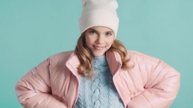 Pembe ceketli ve mavi arka planda kameraya poz veren güzel genç modelin portresi. Genç kız mutlu görünüyor.