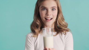 Çekici, gülümseyen sarışın genç kız mavi arka planda bir bardak süt sunuyor.