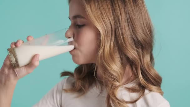 接近金发少女喝牛奶 在蓝色的背景下 有一头乳白胡子在镜头前微笑 — 图库视频影像