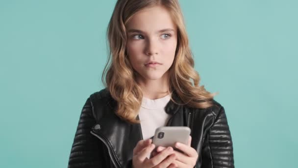 漂亮的金发少女看上去很兴奋 想着如何用智能手机在五彩缤纷的背景下回答信息 现代技术 — 图库视频影像
