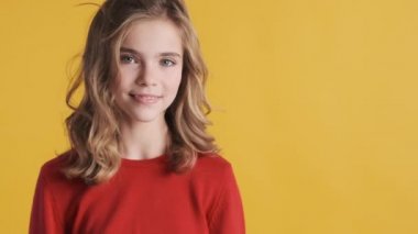 Kırmızı kazak giymiş güzel, neşeli sarışın genç kız sarı arka planda büyüleyici bir poz veriyor.