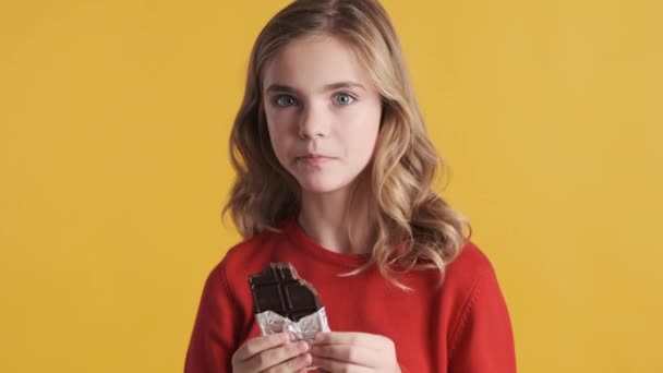 Linda Menina Adolescente Loira Gananciosamente Comer Chocolate Sobre Fundo Amarelo — Vídeo de Stock