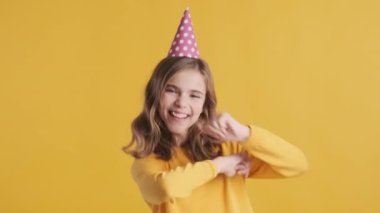 Sarı arka planda doğum gününde parti şapkası takan neşeli sarışın kız. İfade etrafında dolaşmak