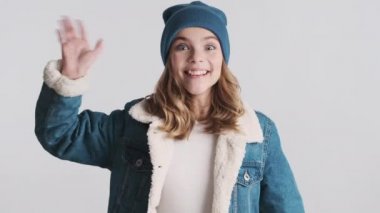 Şapka ve kot ceket giymiş güzel sarışın genç kız ellerini açtı ve beyaz arka planda izole edilmiş kameraya sarıldı. Gel bana, sana sarılmak istiyorum. El sallayan genç kız