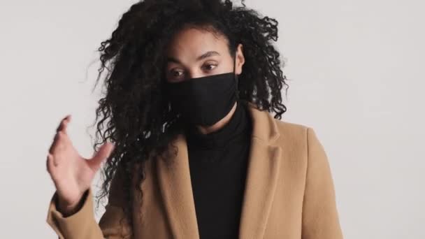 白い背景の上にカメラに黒い医療マスクを着たアフリカ系アメリカ人女性の肖像 安全第一コンセプト — ストック動画