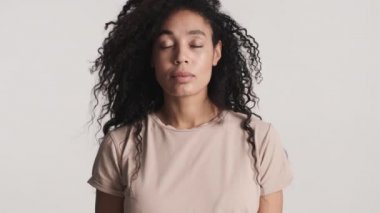 Genç, kabarık saçlı, Afro-Amerikan kadın derin bir nefes alıyor. Beyaz arka planda sakin görünüyor.