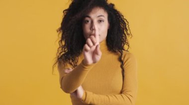 Siyah kabarık saçlı, kendine güvenen genç Afrikalı Amerikalı kadın sarı arka planda parmaklarıyla sayıyor. Jest sayılıyor