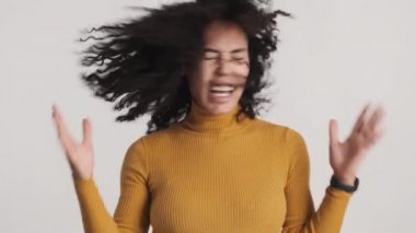 Siyah tüylü, başı sallanan ve beyaz arka planda kameraya gülümseyen duygusal Afro kadın.