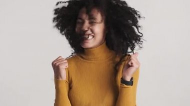 Siyah kabarık saçlı, beyaz arka planda kameraya sevinç saçı sallayan neşeli Afrikalı Amerikalı kadın. Mutlu kız.